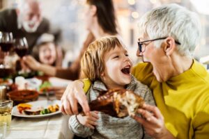 Happy boy and his grandmother having fun while about to eat turkey leg during family's lunch at home.